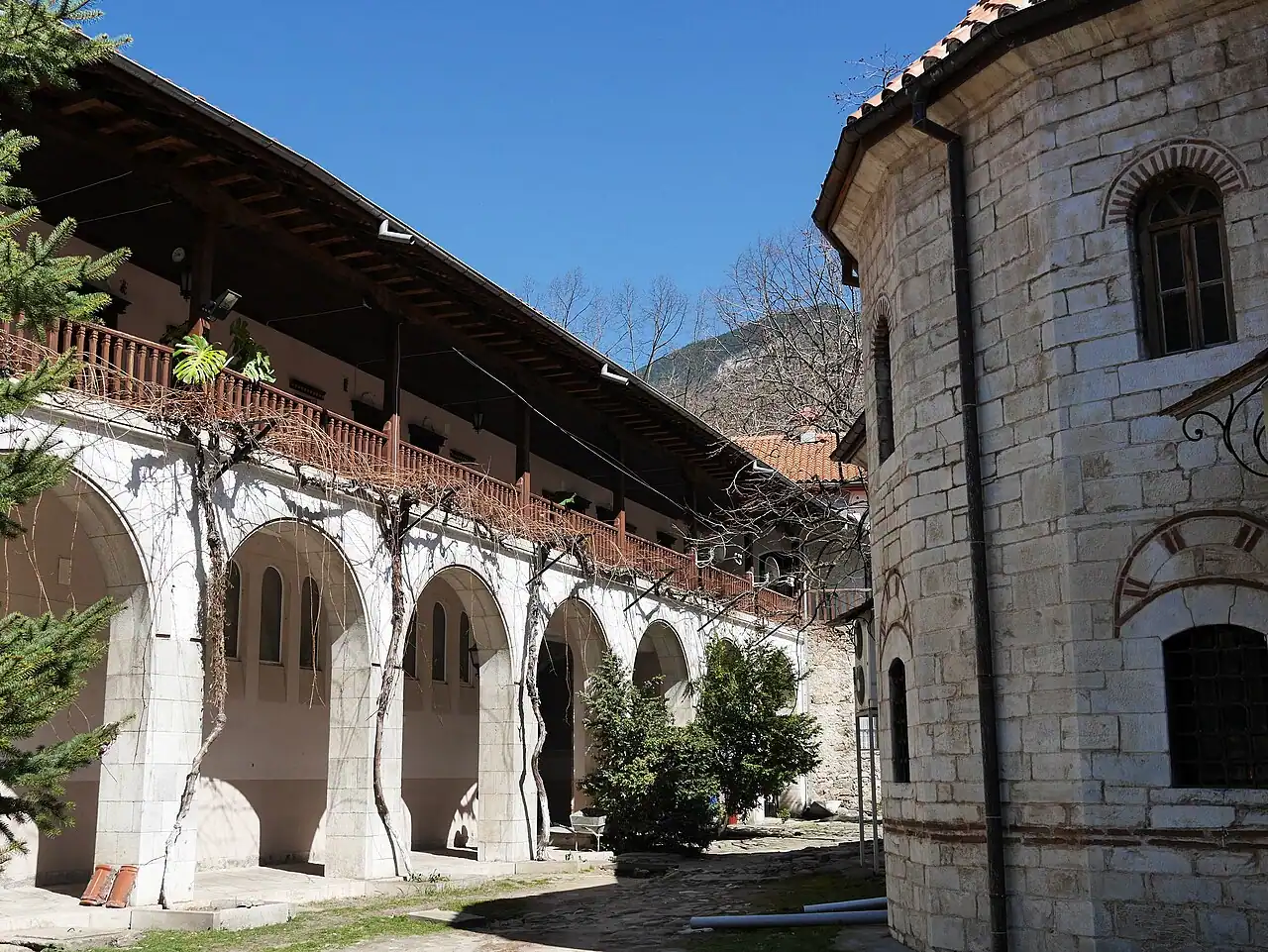 The arcaded galleries and stone church of Bachkovo Monastery in its courtyard, with a Rhodope mountain behind