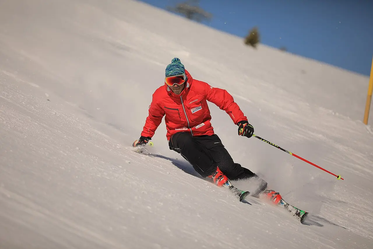 A ski instructor in red jacket teaching a student on a gentle Bansko slope