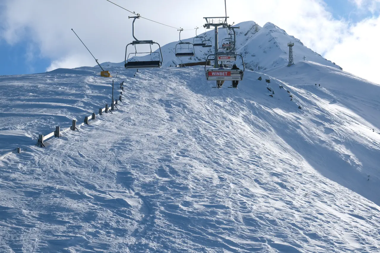 A chairlift climbing toward the bare snow-covered summit of Todorka peak above the tree line at Bansko