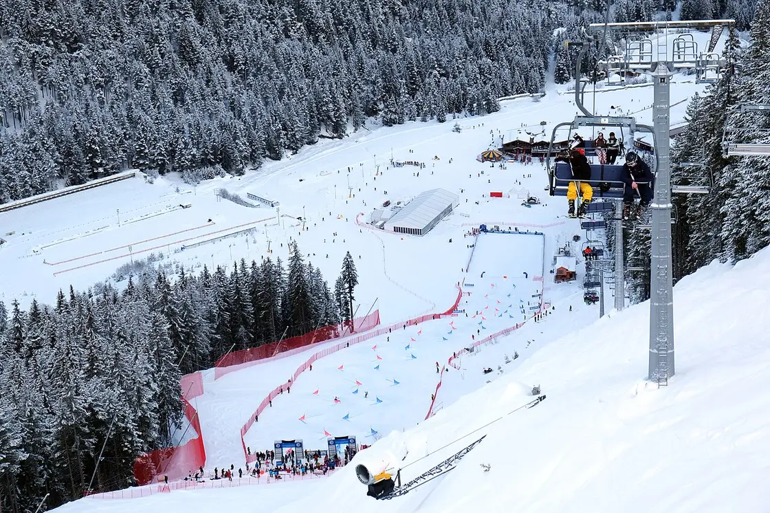 Empty ski chairs climbing a snowy Bansko slope with forest and mountains in the background