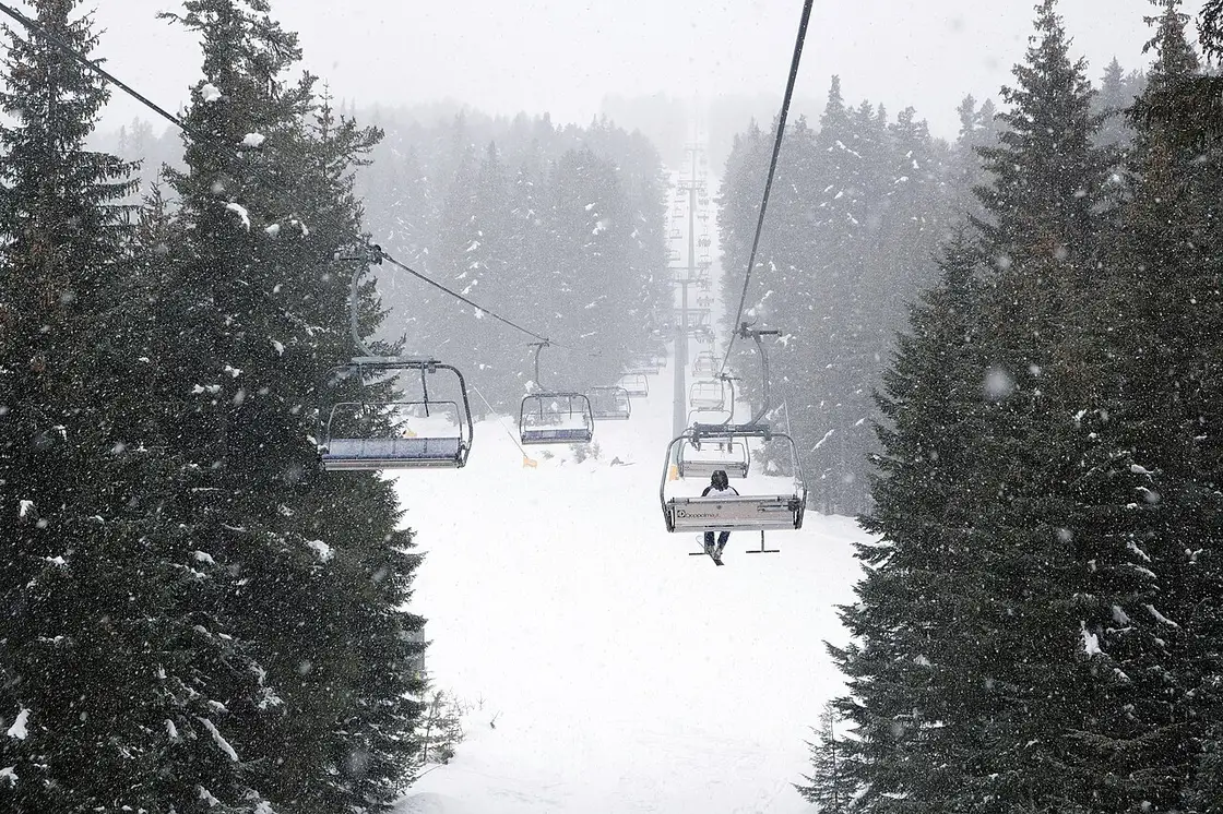 A Doppelmayr chairlift climbing through heavy snowfall between snow-laden spruce trees at Bansko
