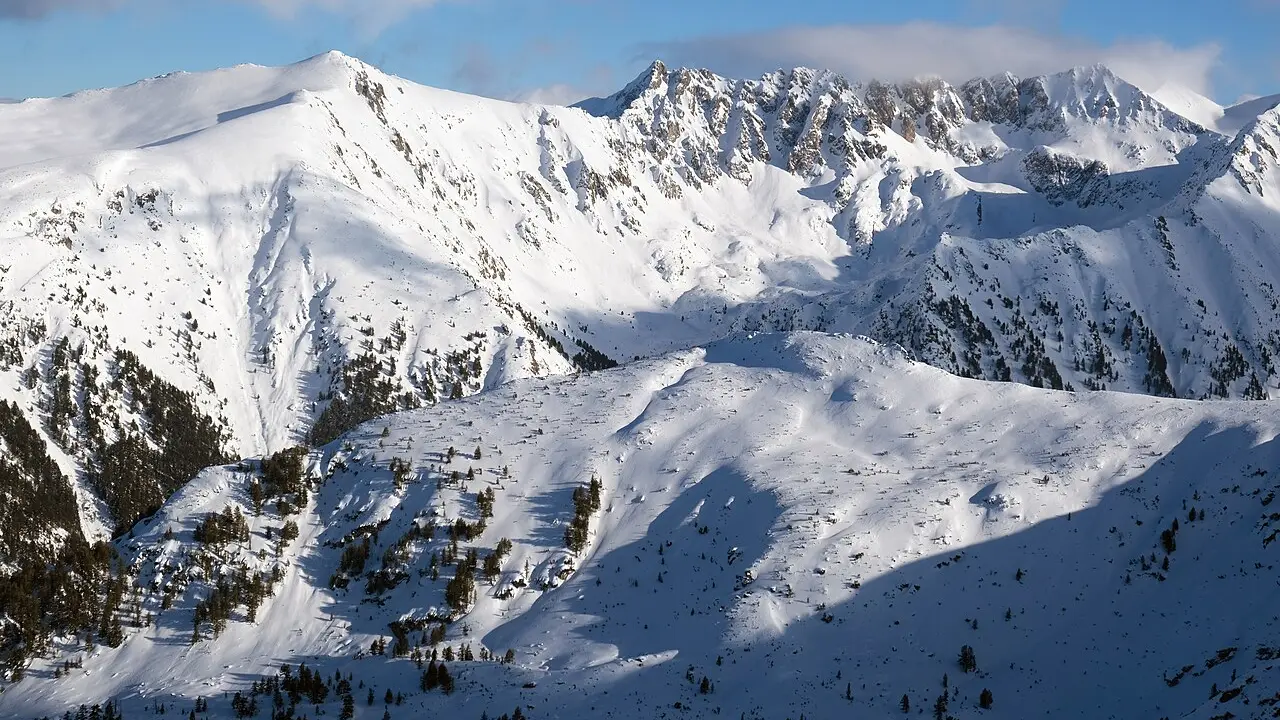 Snow-covered Pirin ridges and rocky peaks above the treeline under a bright winter sky near Bansko