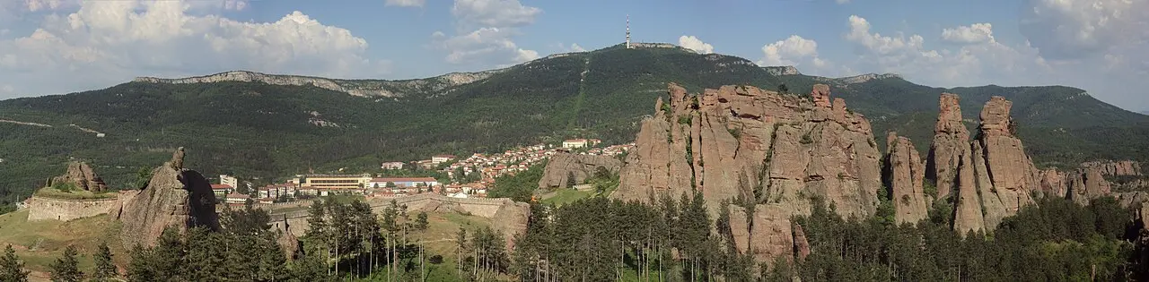 Panorama of Belogradchik: the town below wooded hills with the red rock formations and fortress spread across the ridge