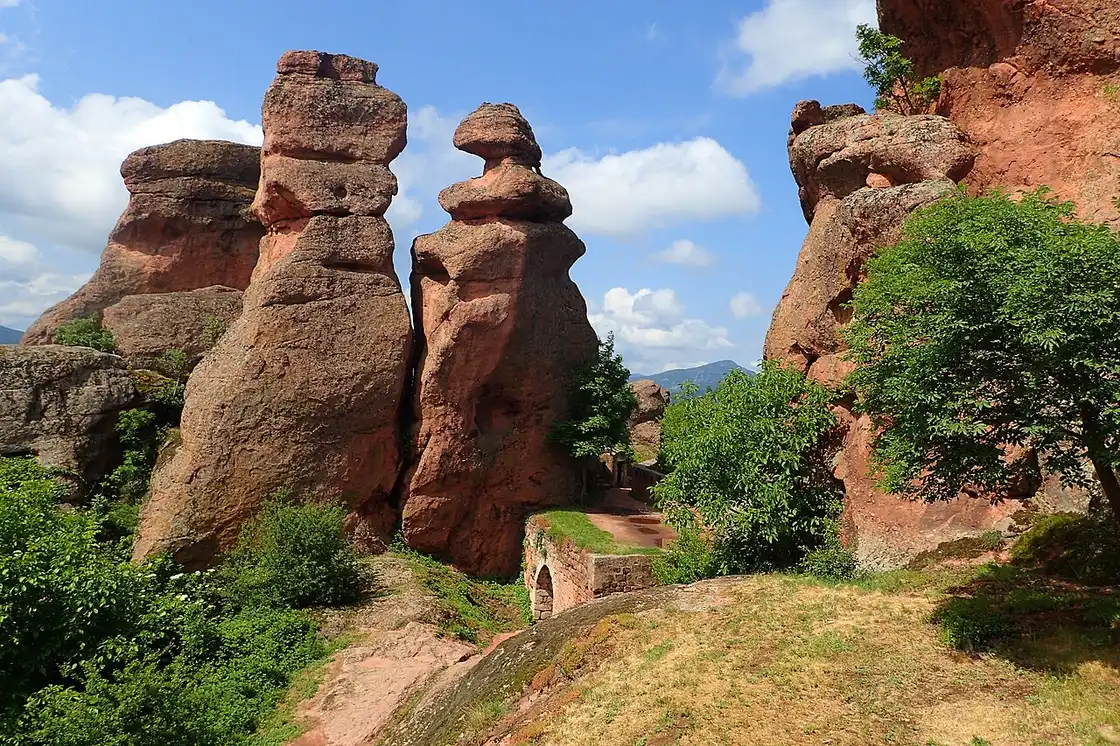 Close-up of the red sandstone rock pinnacles of Belogradchik, weathered into rounded stacked shapes with green trees between them