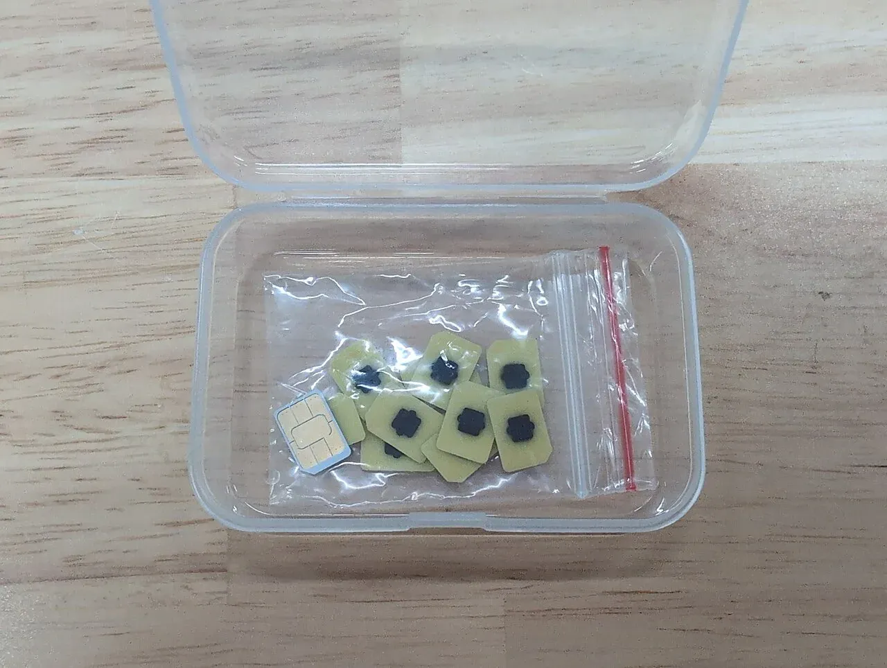 A handful of small eUICC eSIM chips in a plastic bag next to a physical nano-SIM card for scale