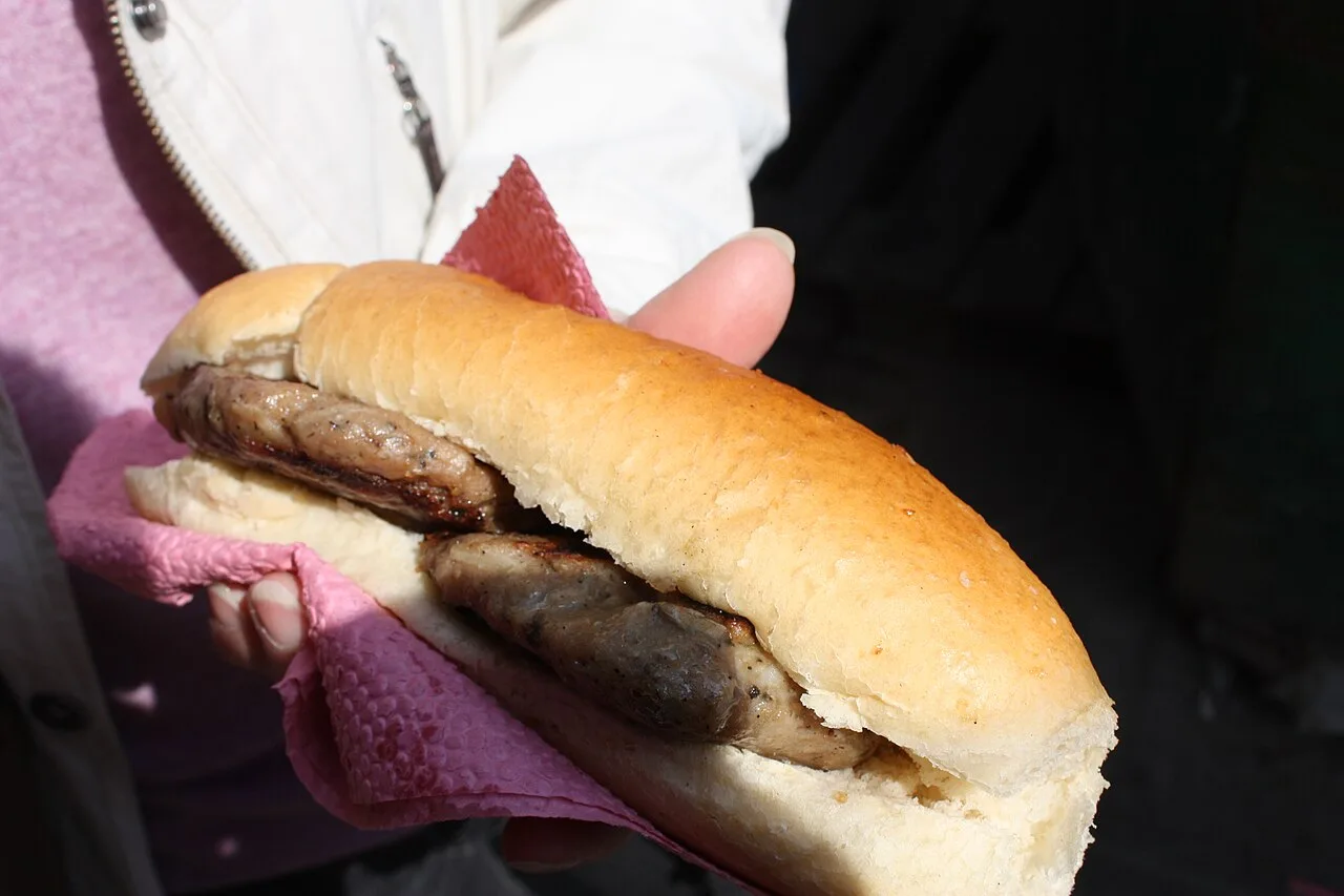 A grilled kyufte, a Bulgarian minced-meat patty, tucked into a soft white bun held in a paper napkin as street food in Sofia