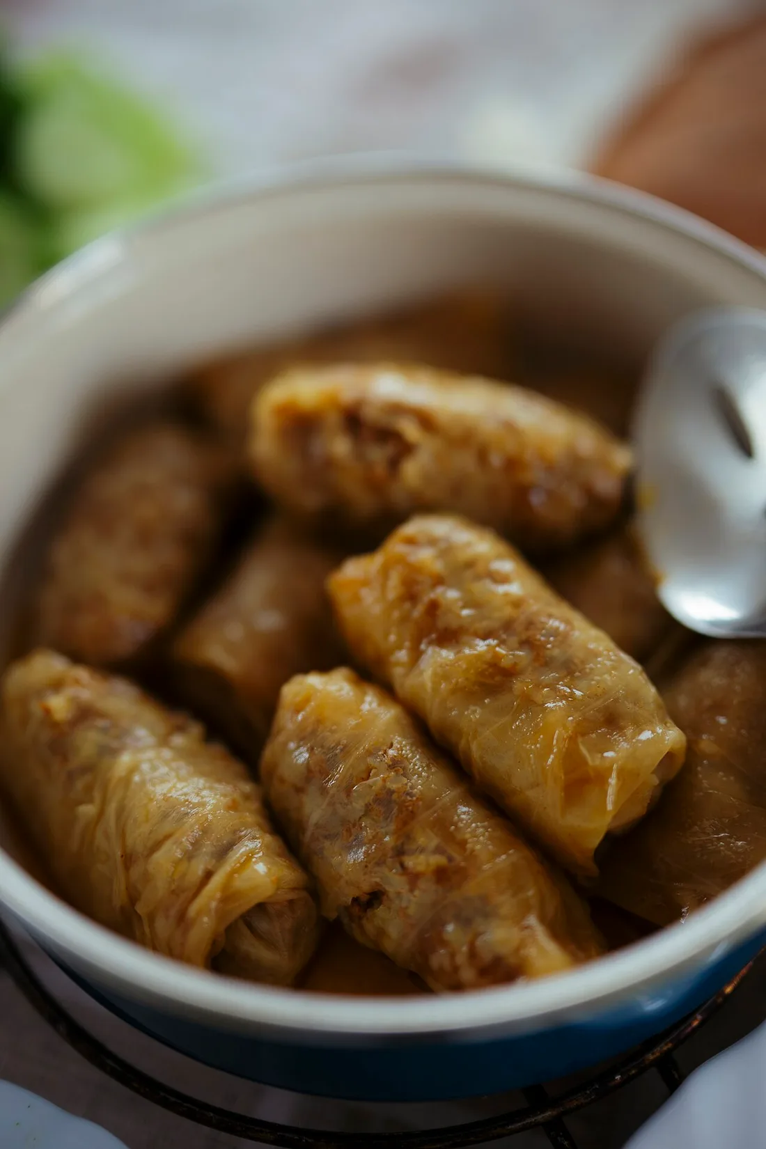 A pot of sarmi, cabbage leaves rolled around a rice and meat filling, in a rich sauce with a serving spoon