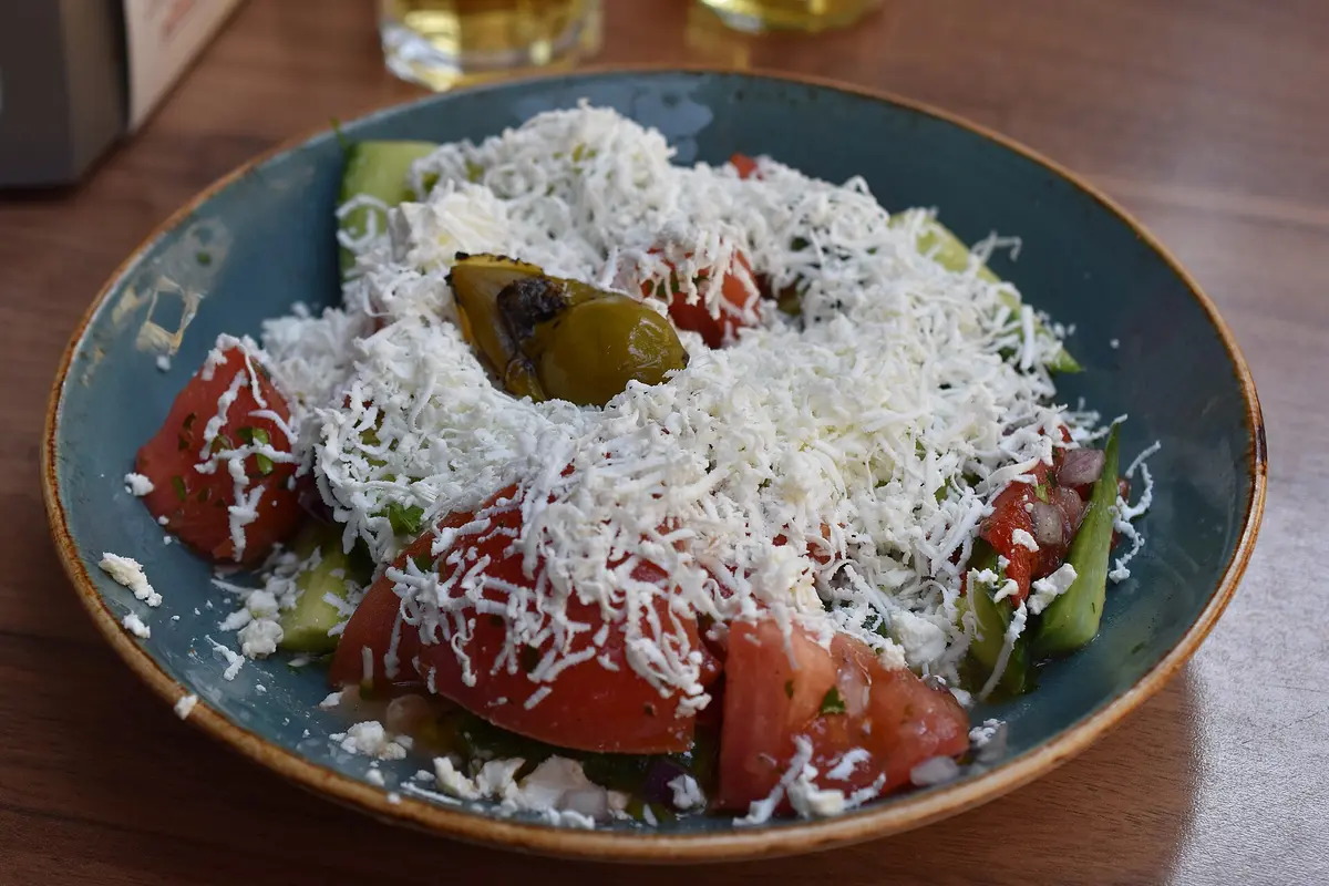 A shopska salad of tomatoes, cucumbers and grated white cheese in a white bowl