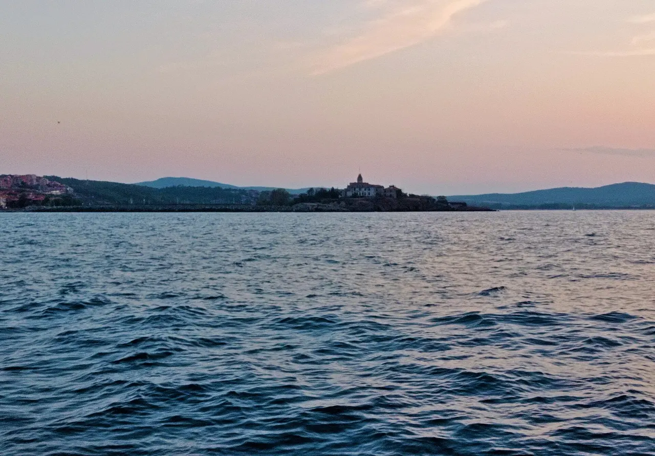Sozopol old town on its rocky peninsula seen from the sea, red roofs packed above the water