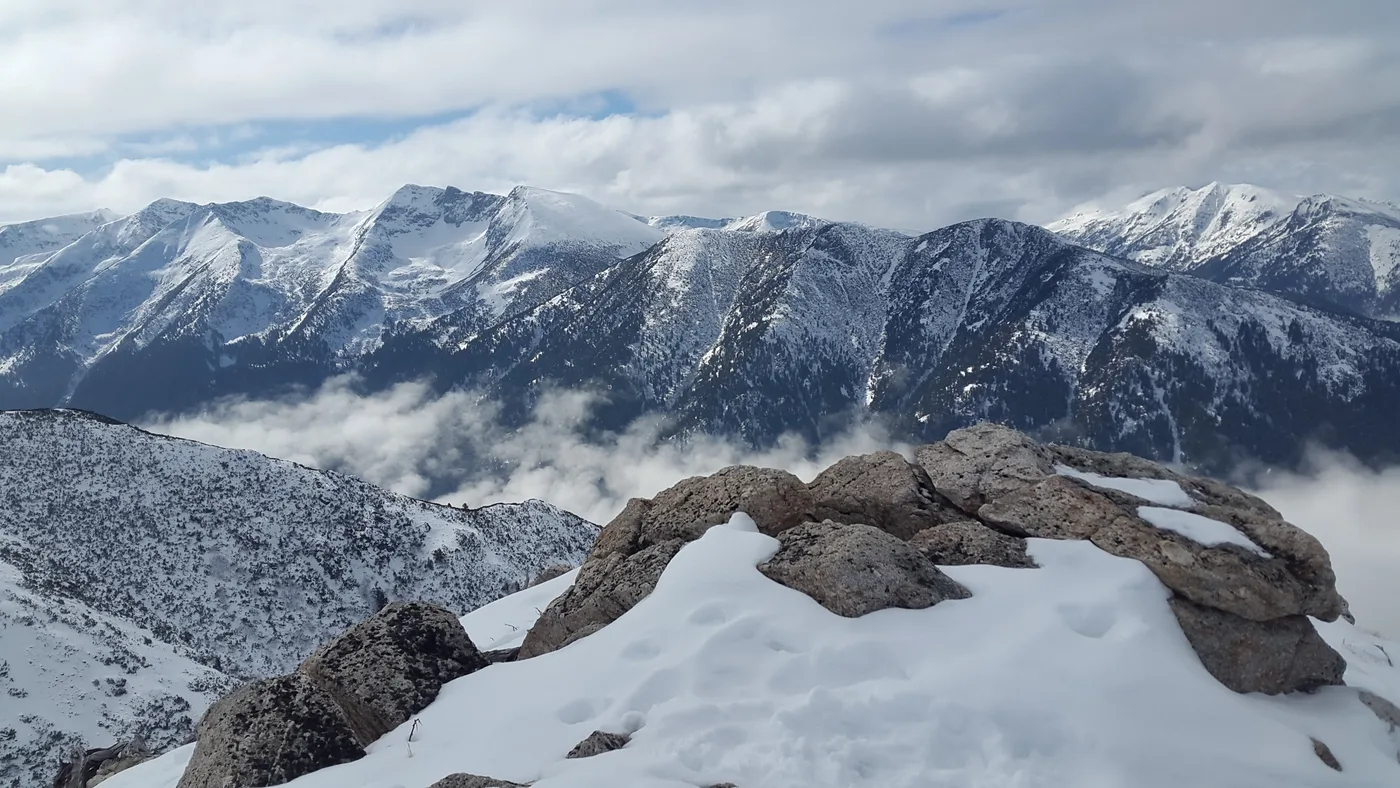 Snow-covered peaks of the Rila mountains under scattered cloud, ridgelines and forested slopes stretching to the horizon