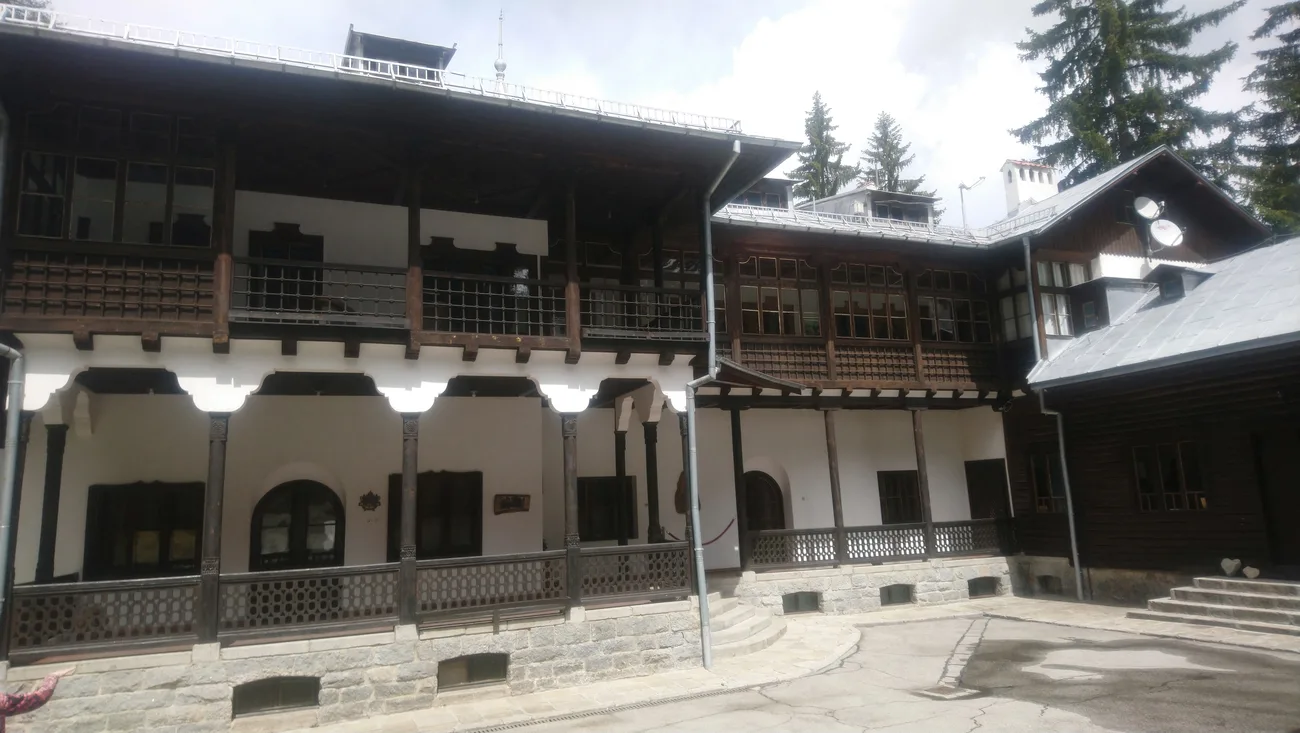 The timber-and-white Tsarska Bistritsa royal palace at Borovets, carved wooden balconies and verandas around a stone-paved courtyard