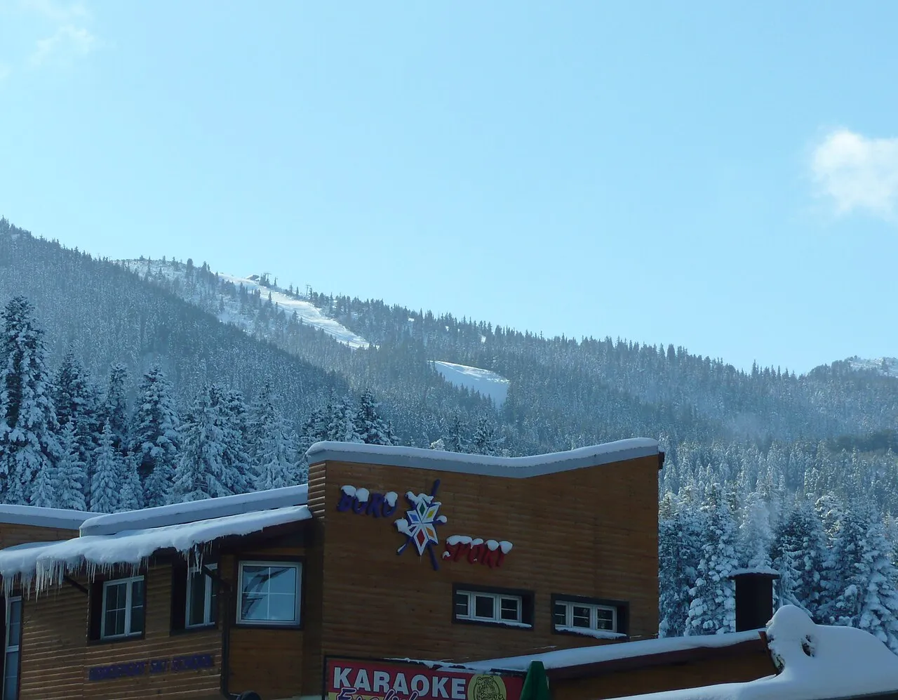 A timber ski-sport building at the Borovets base with a piste and lift line visible cutting up the snowy mountain behind it