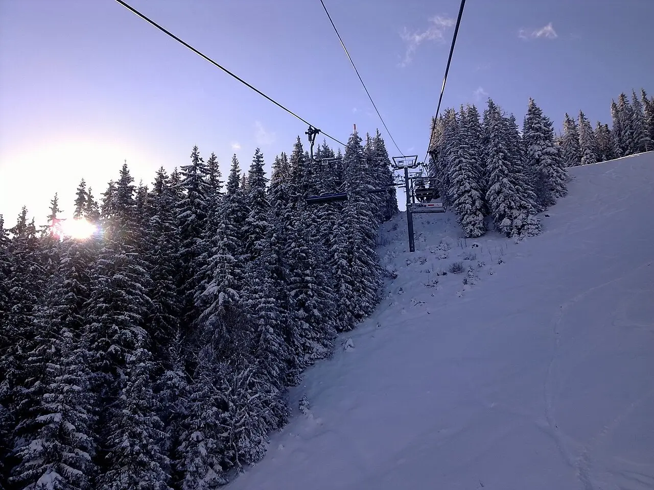 Riding a chairlift through snow-laden spruce trees at Pamporovo with low winter sun flaring through the branches