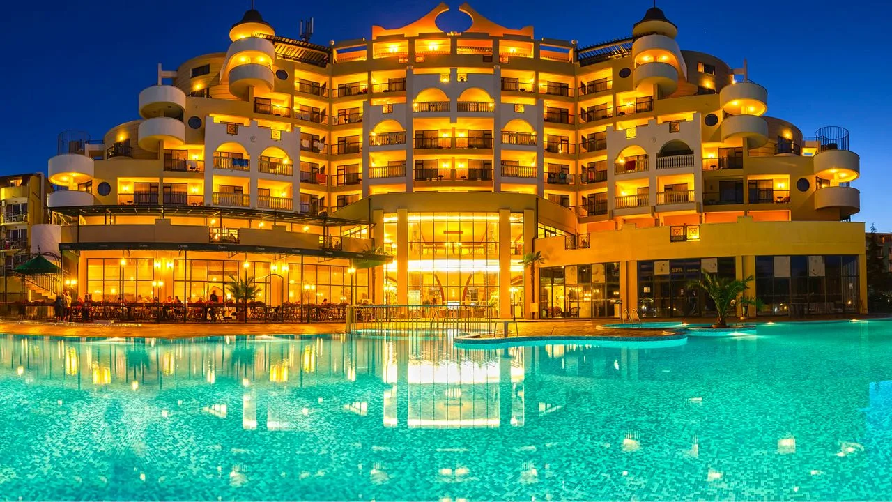 A large all-inclusive hotel at Sunny Beach lit up at dusk, its balconies glowing above a floodlit outdoor pool