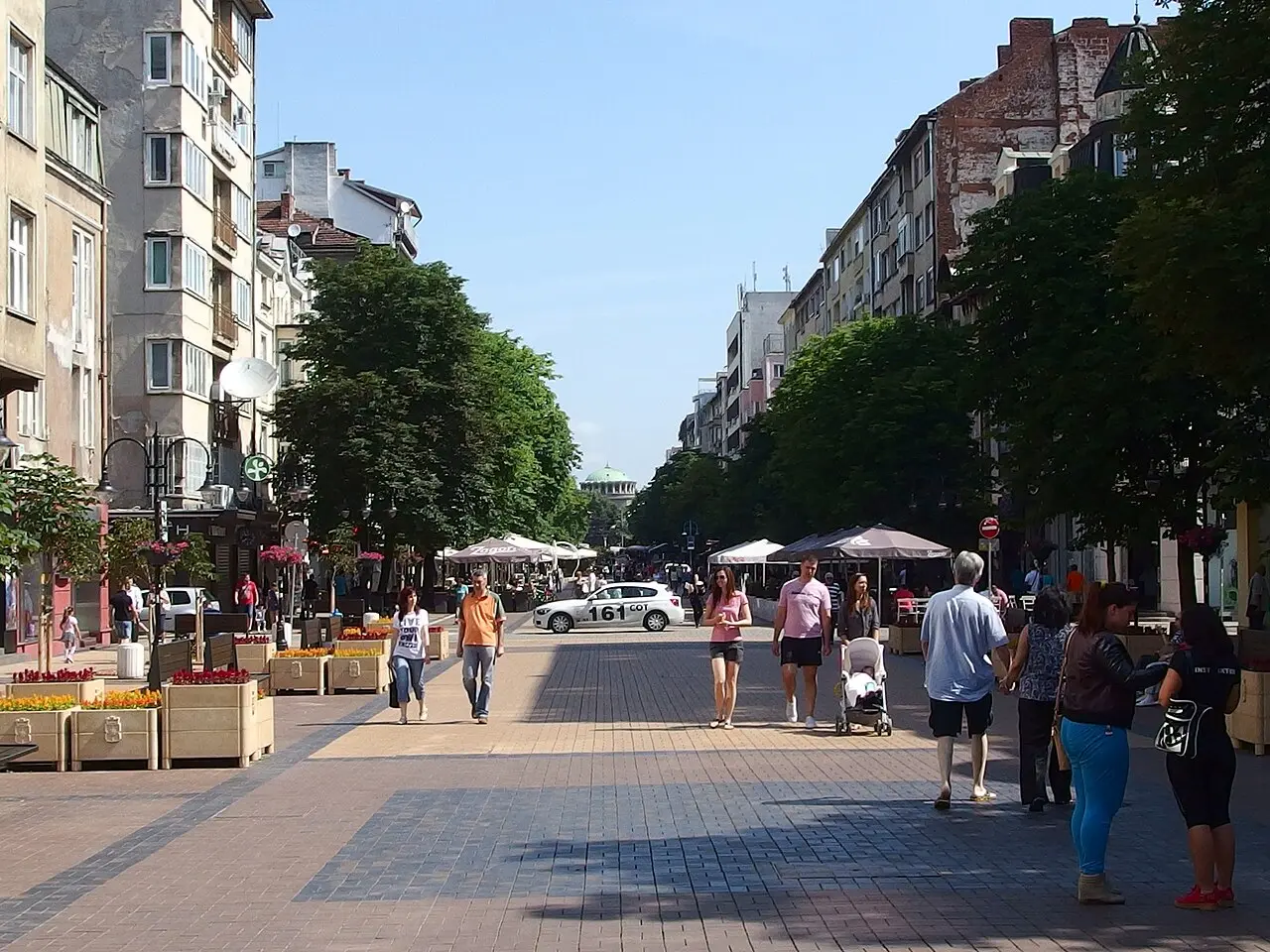 A pedestrian street in central Sofia with cafe umbrellas, trees and people walking on a summer afternoon