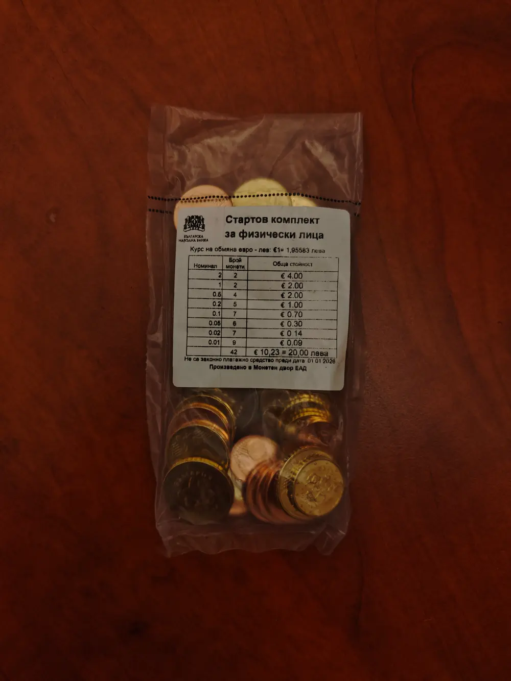 A clear plastic bag of Bulgarian euro coins on a wooden table, the label showing the fixed rate 1 euro equals 1.95583 leva and a breakdown of 10.23 euro equals 20 leva
