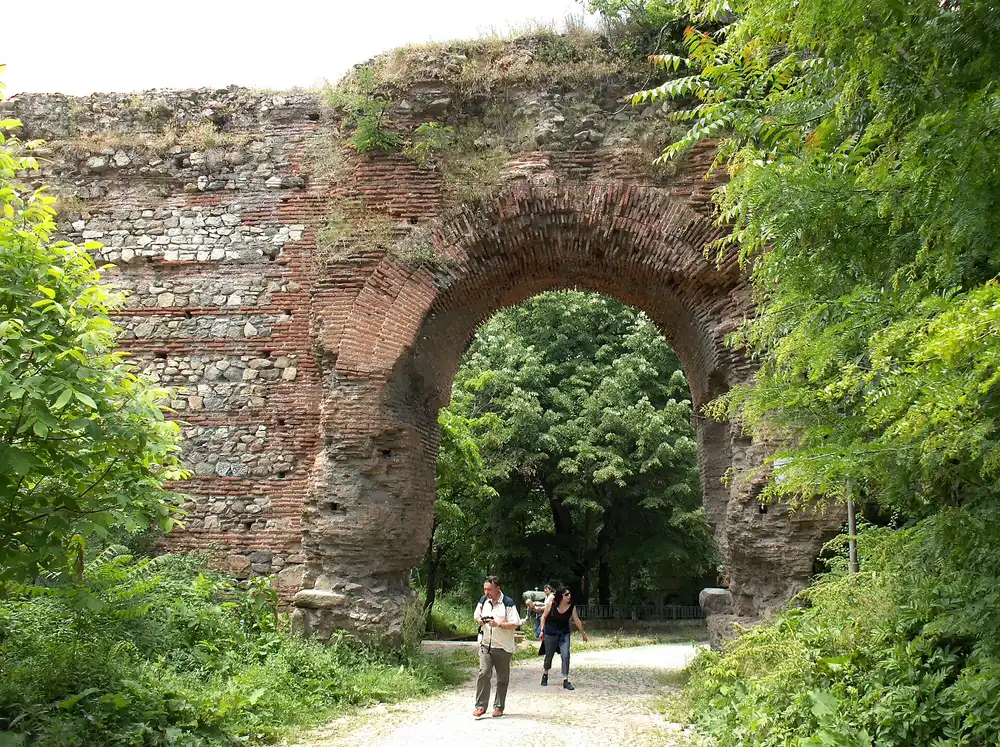 The tall brick-and-stone Roman arch known as the Camels gate at Hisarya, part of the surviving fortification wall, with two people walking beneath it