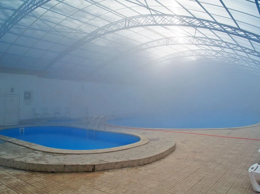 Steam filling a covered mineral-water pool complex in Bulgaria, with a small oval pool in the foreground and a larger one disappearing into the mist