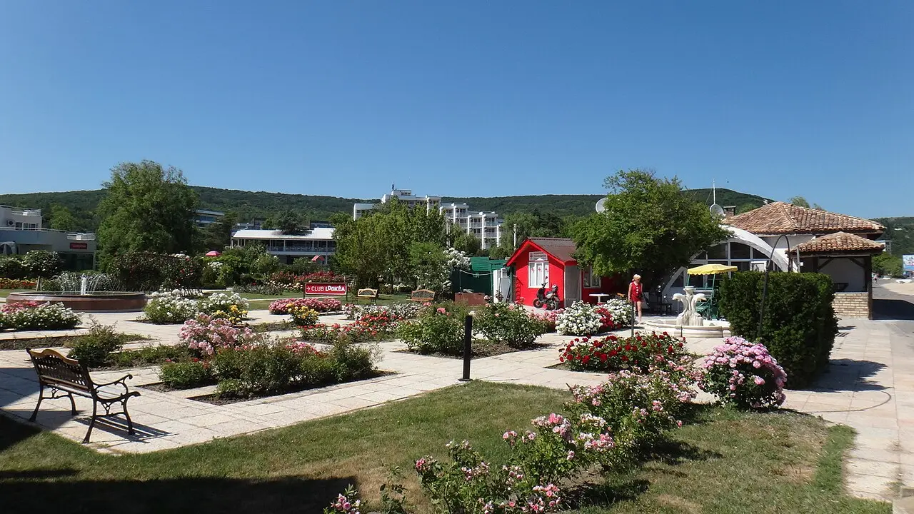 Manicured resort gardens at Albena with rose beds, a fountain and low hotels backed by green hills, no cars in sight
