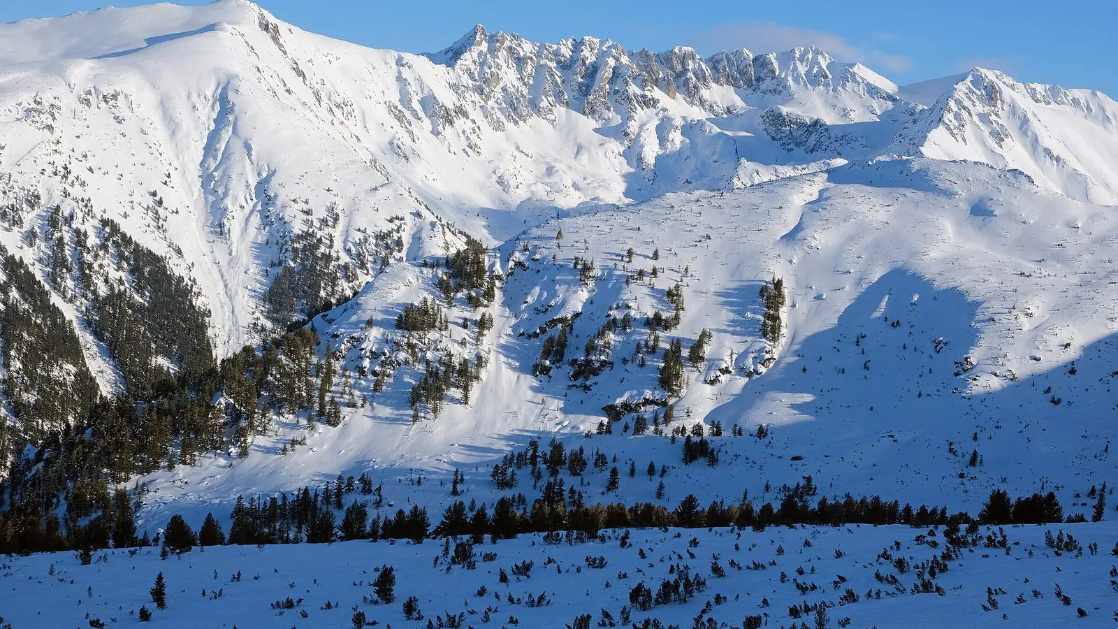 Skiers on a wide groomed piste at Bansko with a chairlift and snow-covered Pirin ridges behind