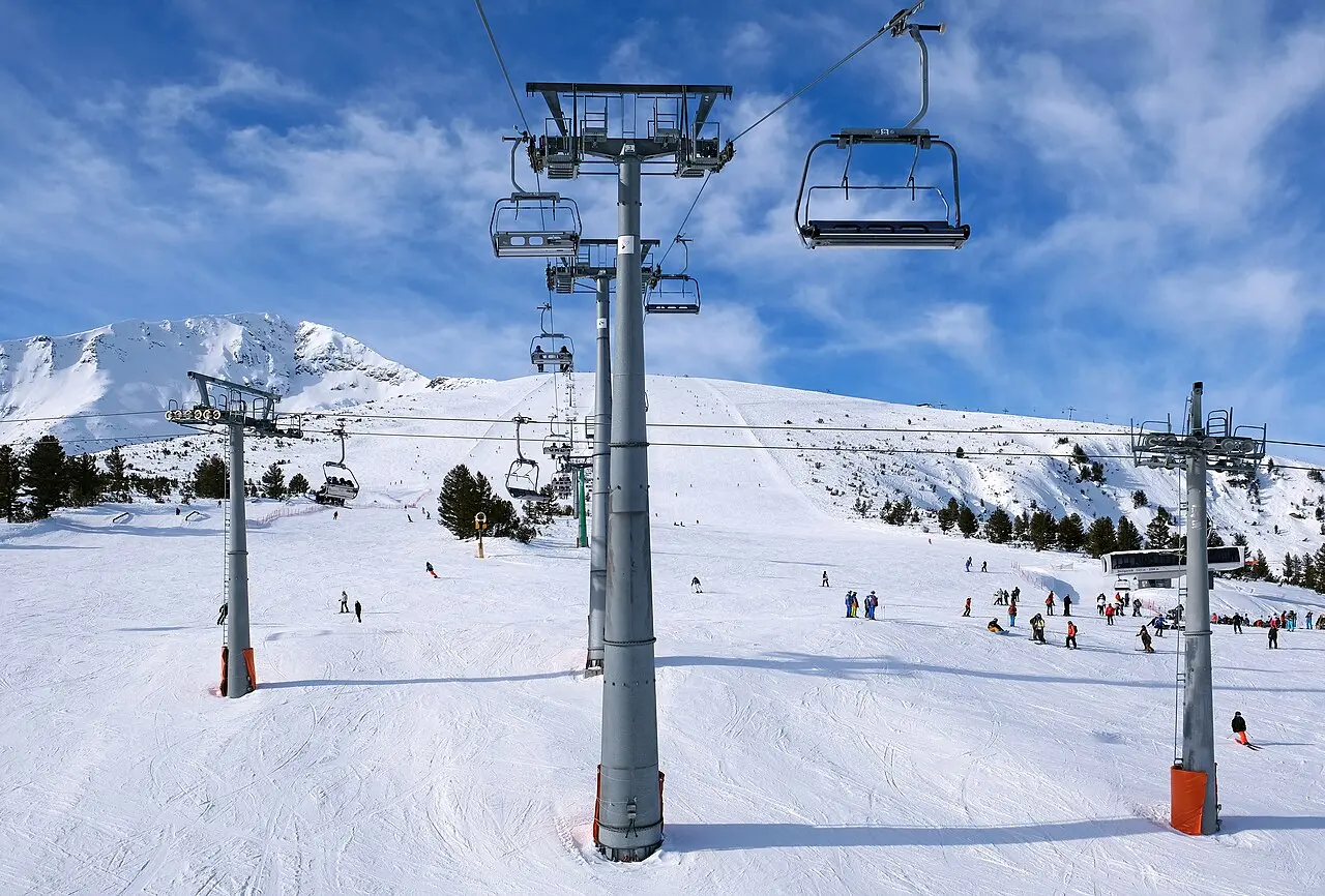 Three chairlift towers on a wide open piste near the treeline at Bansko with a mountain ridge behind