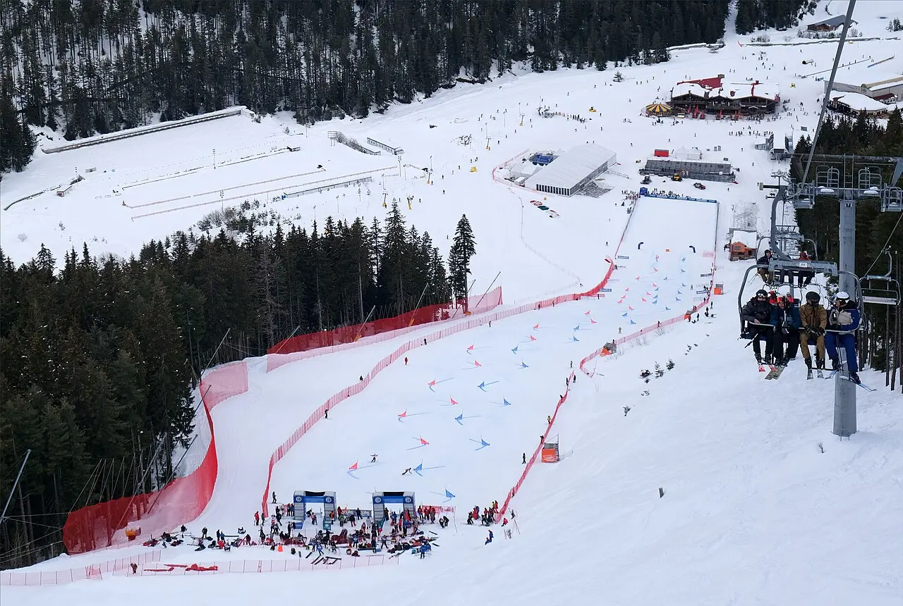 Red safety netting marking both sides of a World Cup race piste at Bansko, with a chairlift and skiers passing above