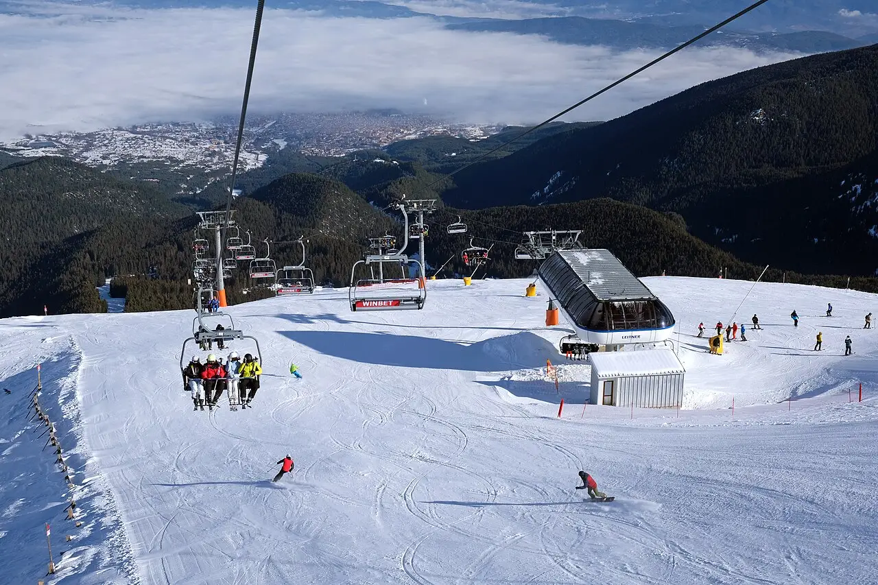 A piste and chairlift high above Bansko with the town far below in the valley, partly hidden in cloud