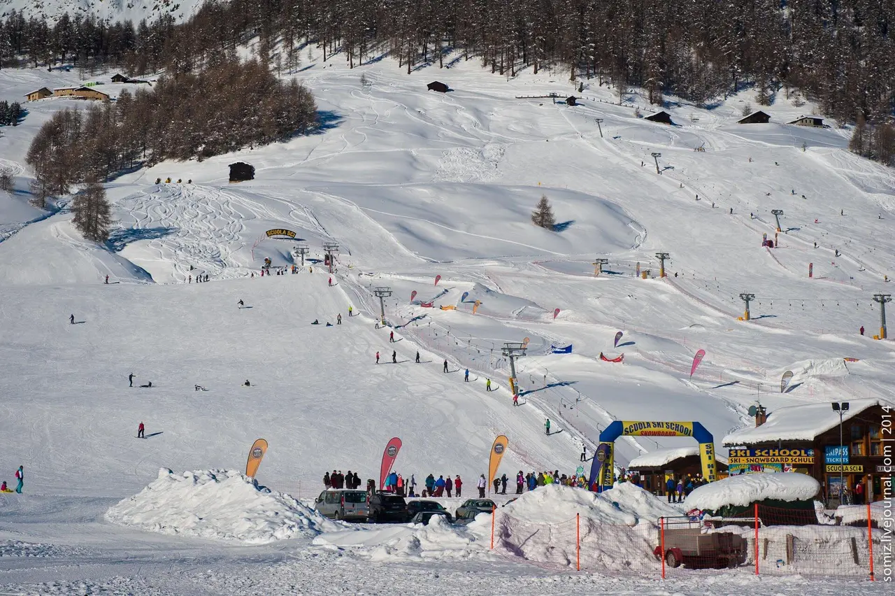 The base area of a Livigno ski slope with skiers, a ski-school tent and chairlifts running up the mountain