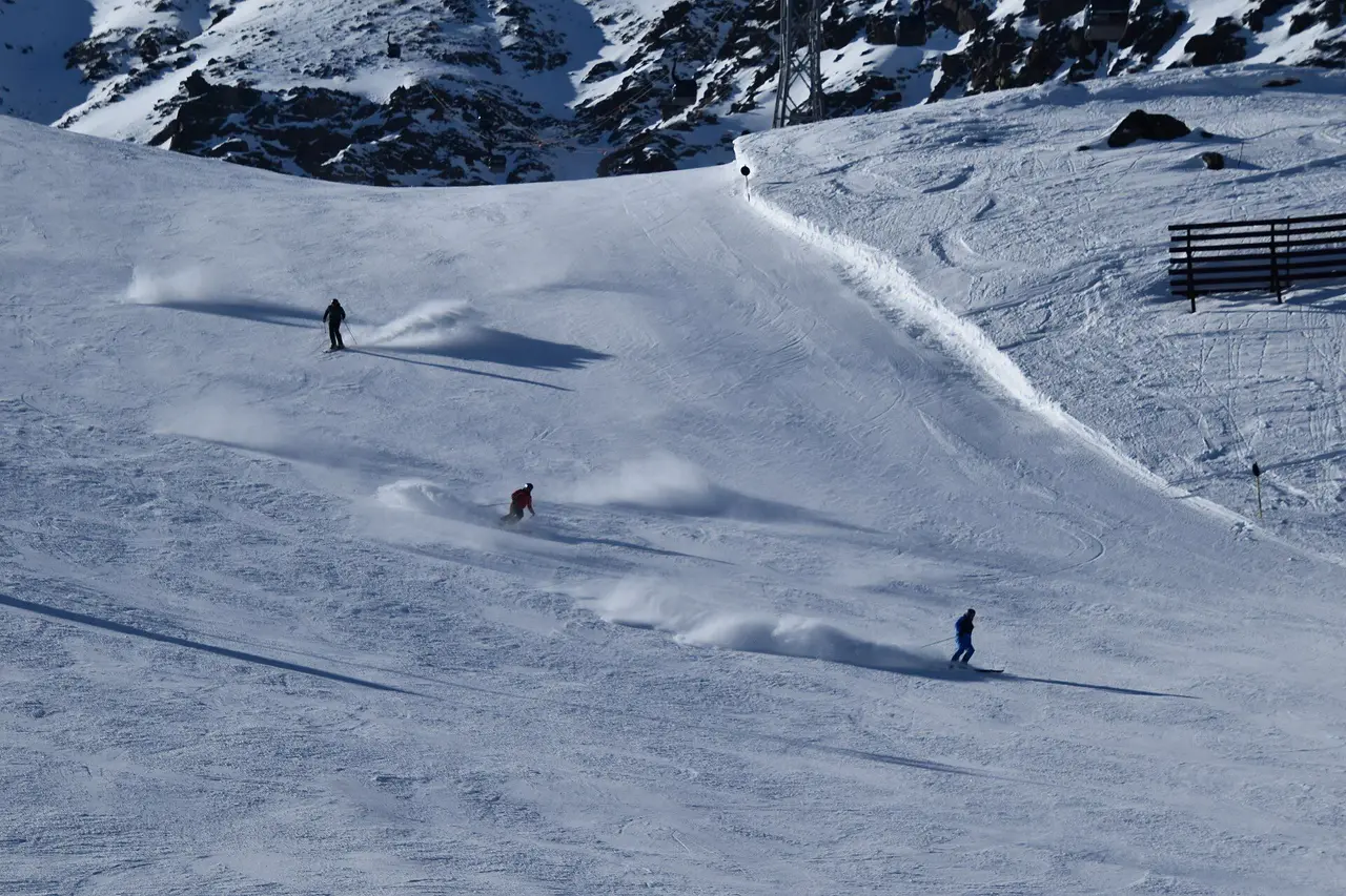 Skiers descending an open high-altitude bowl above the treeline near Sölden with jagged peaks behind