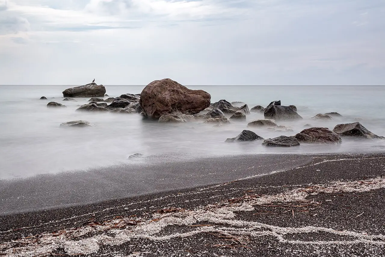 Dark volcanic cliffs and a wide grey sand beach at Vlychada on Santorini with calm Aegean water