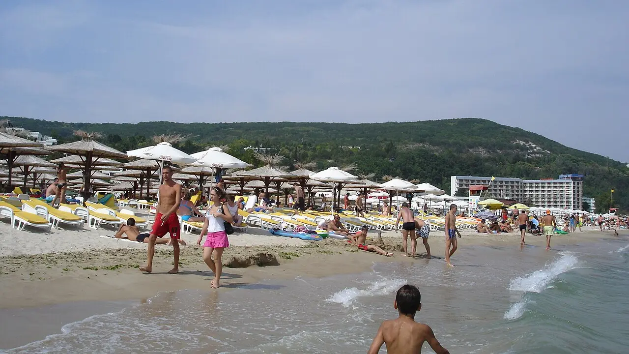 The wide sandy beach at Albena with low-rise hotels set back among pine trees and calm shallow water along the shore