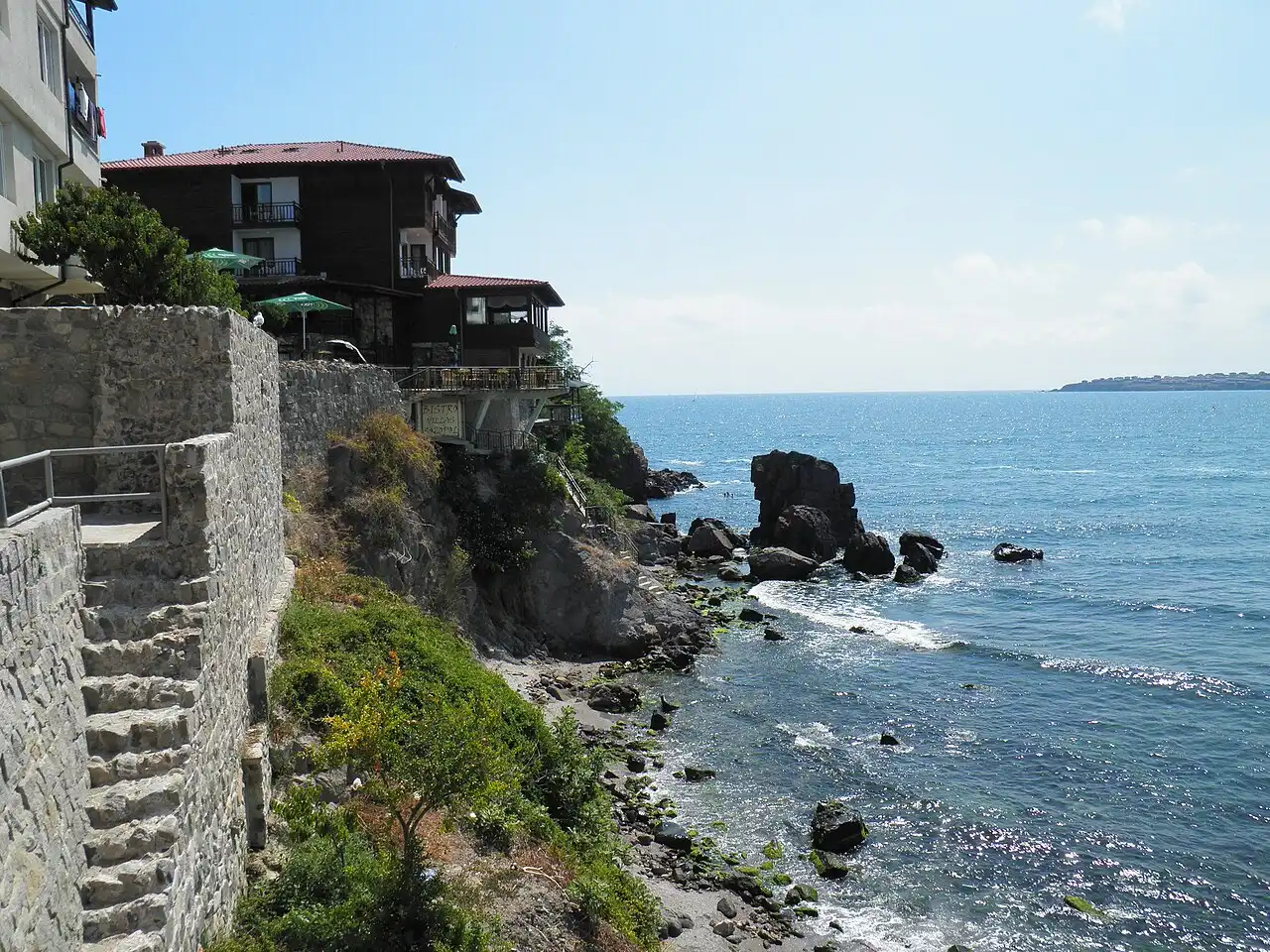 Dark timber old-town houses on the stone sea wall of Sozopol above a rocky Black Sea shore