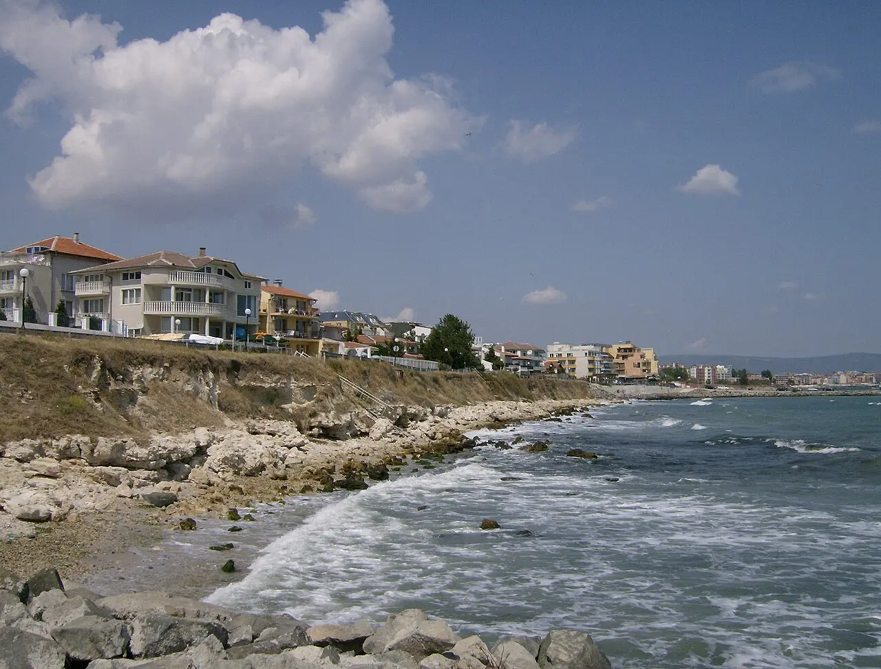 The rocky coast at Ravda with low houses on the shore and the towers of Sunny Beach in the distance