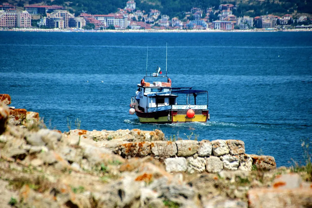 A small fishing boat crossing blue water off Nessebar with the high-rise towers of Sunny Beach on the far shore