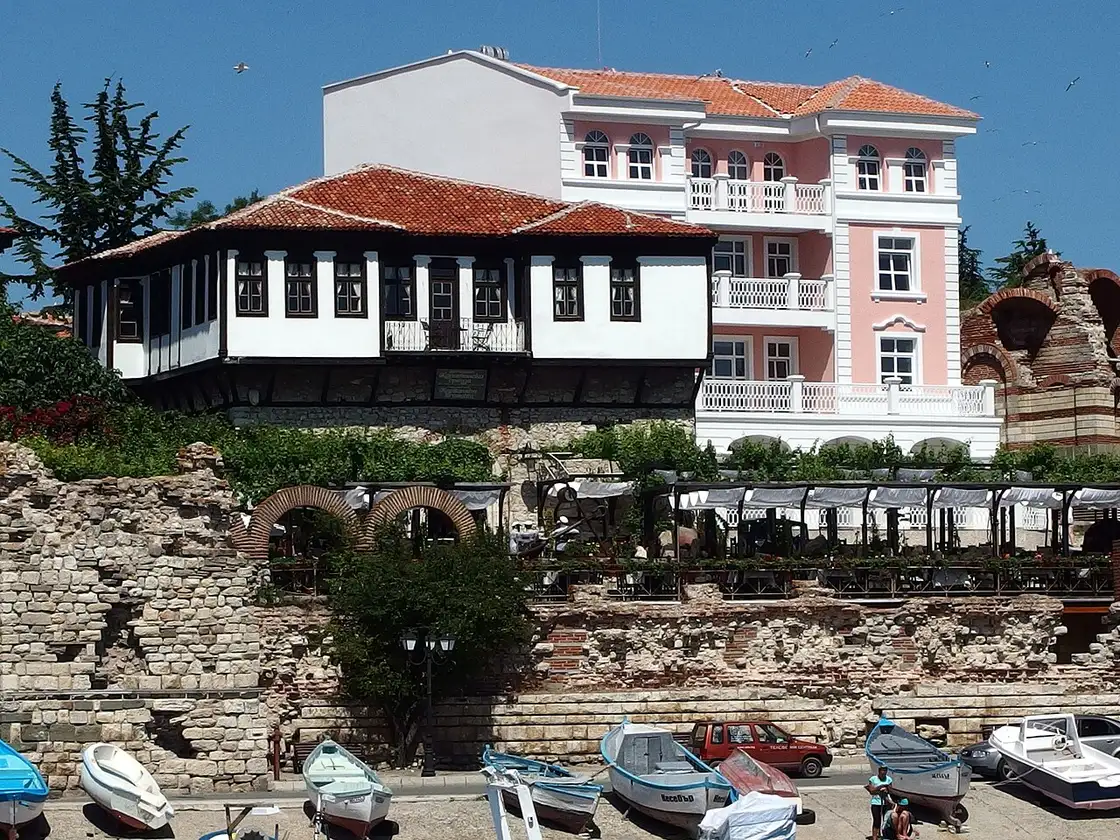 A traditional black-and-timber Nessebar house above ancient stone ruins and fishing boats on the old town shore