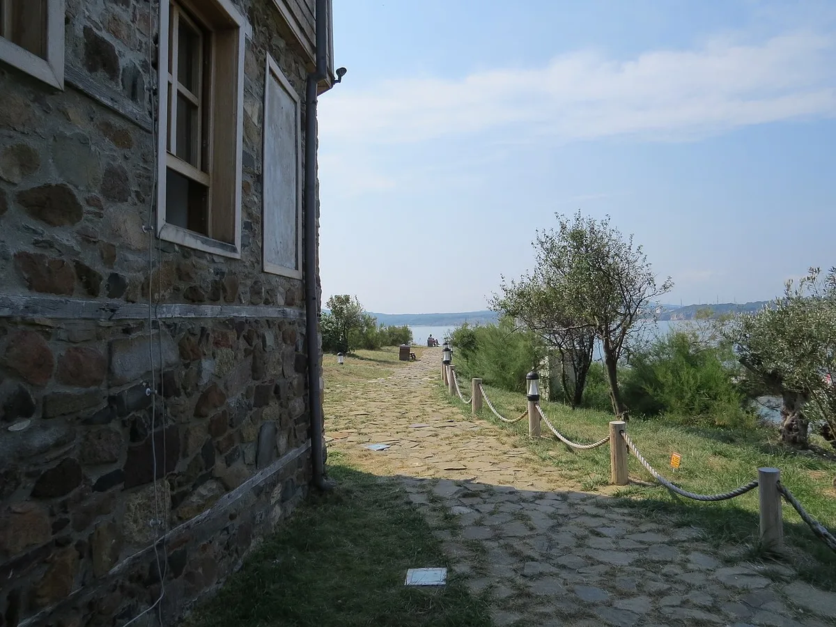 A cobbled lane on St Anastasia Island past a stone house, running down toward the sea with olive trees along the path