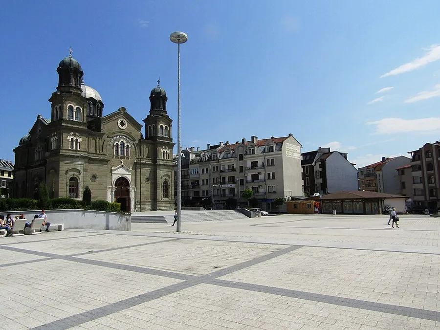The twin-domed Saints Cyril and Methodius Cathedral in Burgas seen across the wide paved Troykata Square under a blue sky