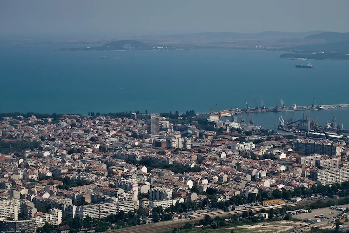 Aerial view over Burgas: red-roofed streets running down to the Black Sea bay and the cargo port, with headlands on the horizon