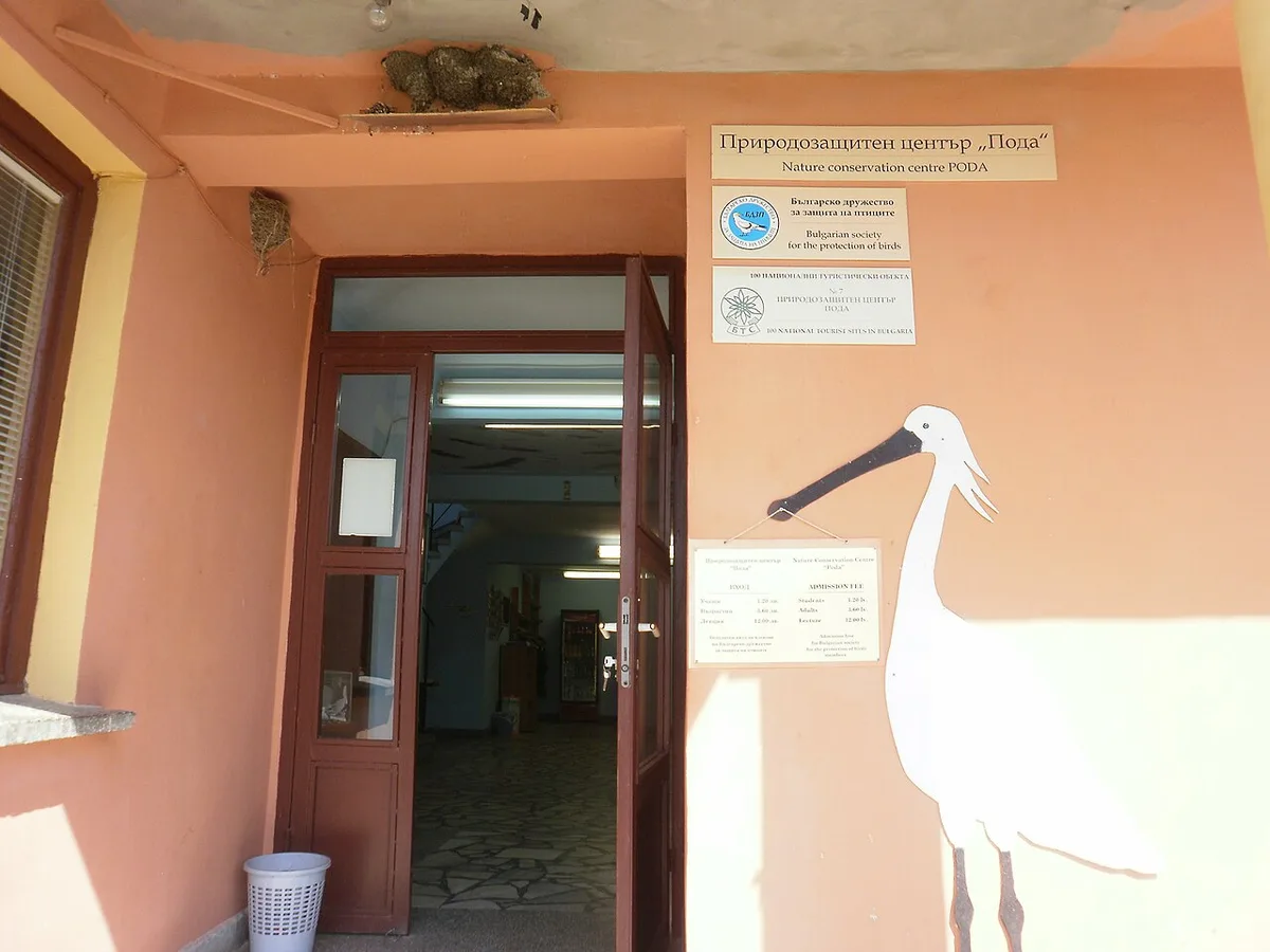 The entrance to the Poda Nature Conservation Centre near Burgas, an ochre building with a bilingual sign and a painted spoonbill on the wall