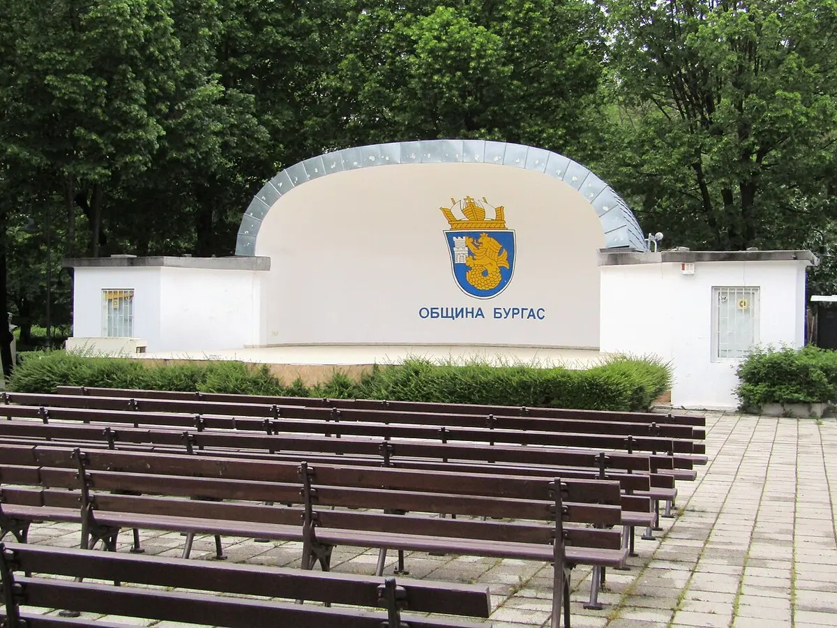 The open-air summer stage in the Sea Garden of Burgas, painted with the city coat of arms, with rows of wooden benches in front