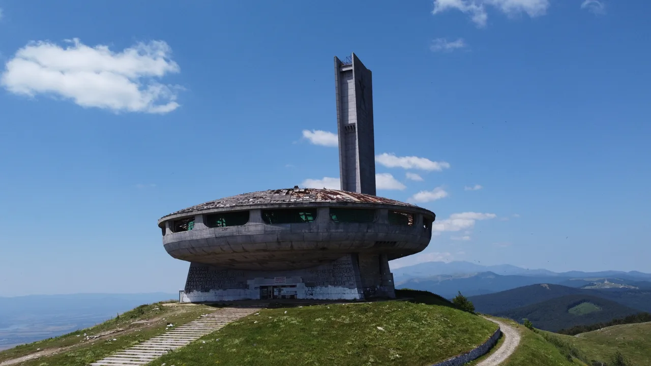 The concrete saucer of the Buzludzha monument with its tall pylon standing on a bare green ridge in the Balkan mountains