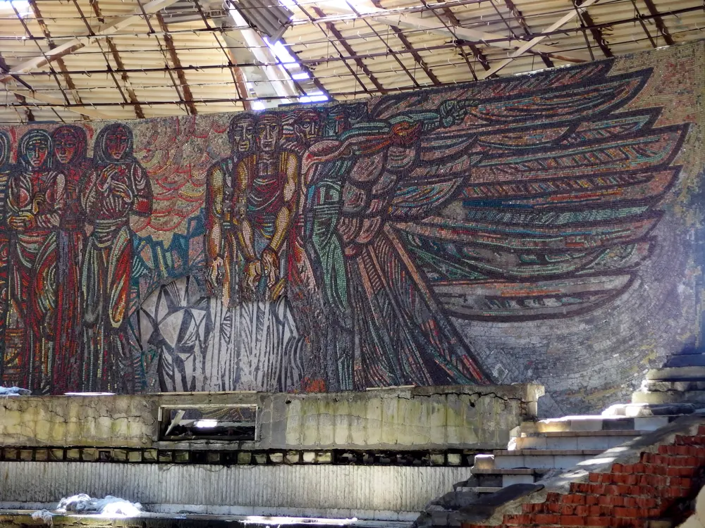A large socialist-realist mosaic panel of winged figures in red, blue and gold on the curved inner wall of the Buzludzha monument