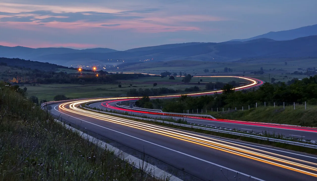 Long red and white car light trails streaking along a Bulgarian highway at dusk with hills in the background