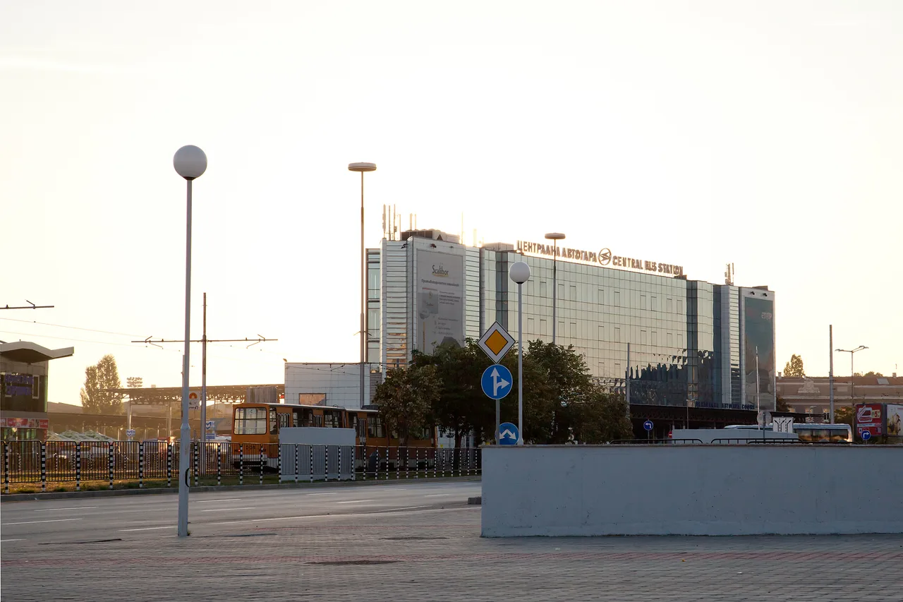 The glass building of the Central Bus Station in Sofia at sunset, with a yellow tram passing in front