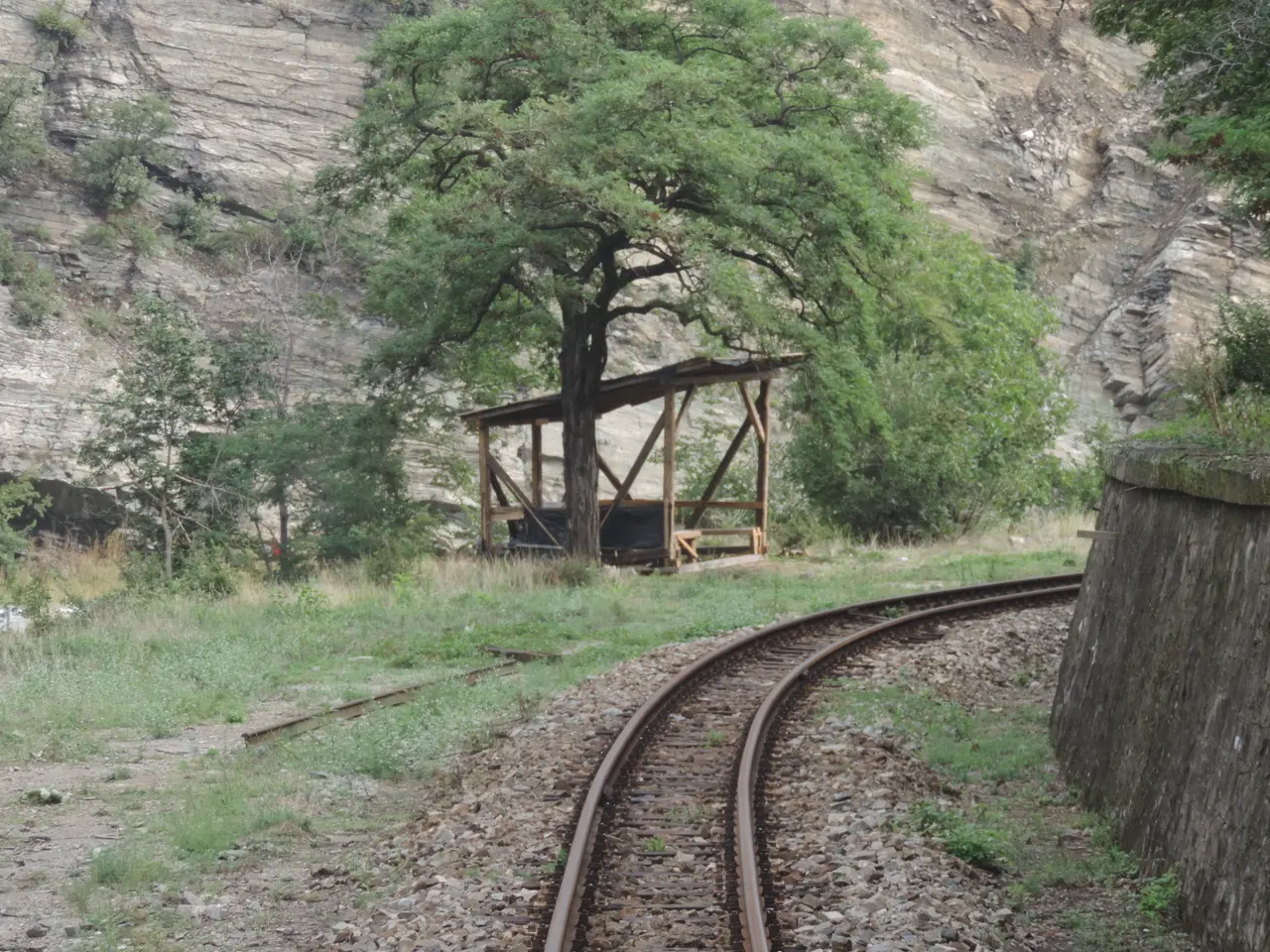 The single narrow-gauge track curving past a rock face and a small wooden shelter in the Bulgarian mountains