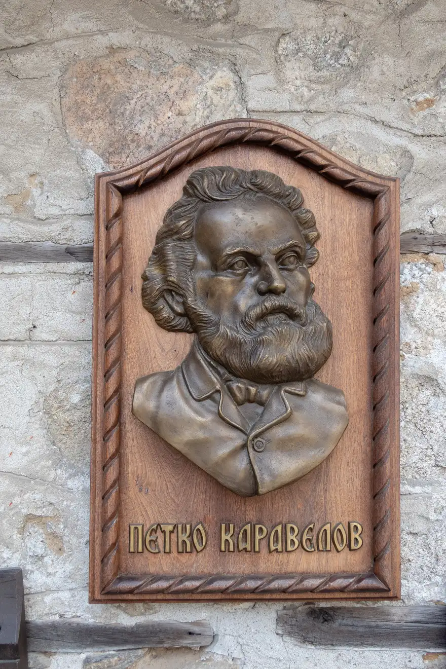 A bronze relief portrait of Petko Karavelov on a carved wooden plaque mounted on the stone wall of the Karavelov house complex in Koprivshtitsa