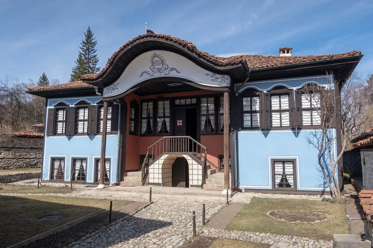 The Lyutov House in Koprivshtitsa: a sky-blue mansion with a curved, wave-shaped baroque pediment over the entrance and a dated 1854 medallion