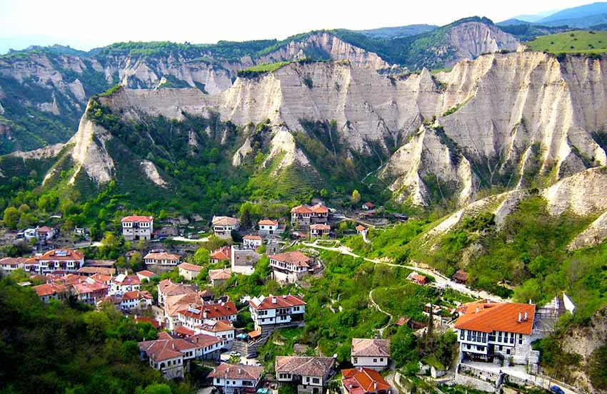The red-roofed houses of Melnik packed into a green valley beneath tall pale sandstone pyramids
