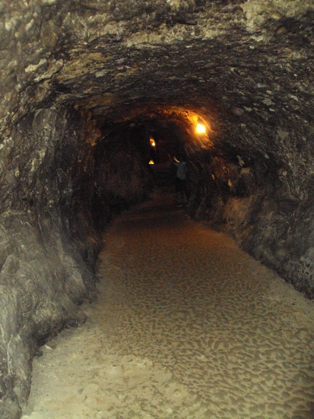 A long dark tunnel dug into the rock beneath the Kordopulov House, lit by a single bulb, with a pebbled floor