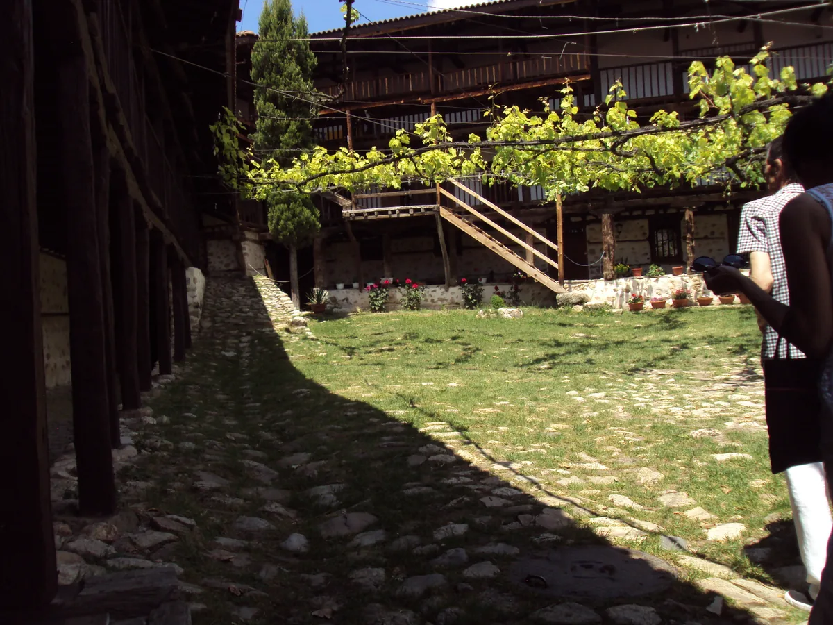 The arcaded wooden galleries and vine-covered courtyard inside Rozhen Monastery, with a cobbled path and flowers